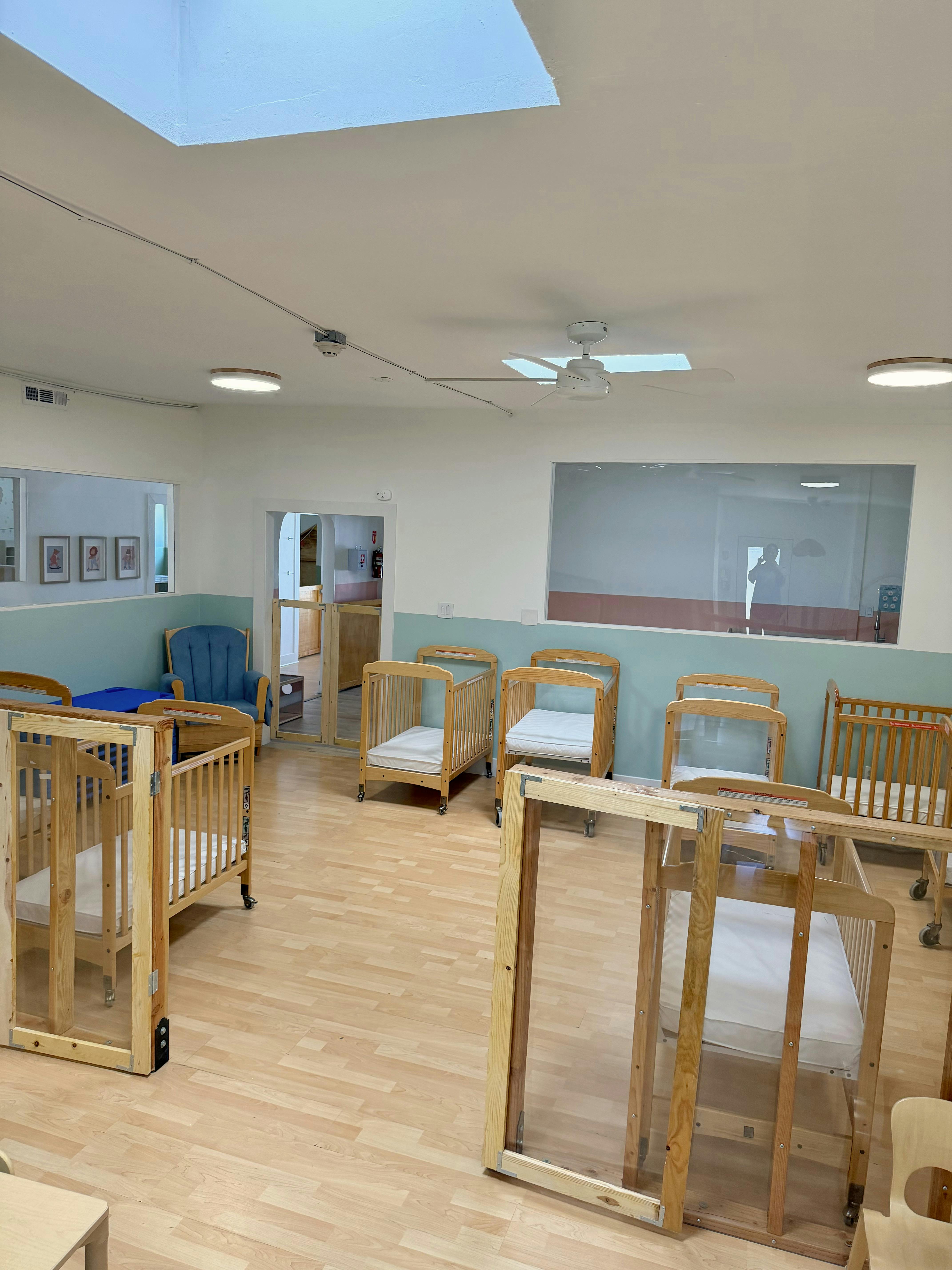 An empty nursery with multiple wooden cribs and a blue rocking chair