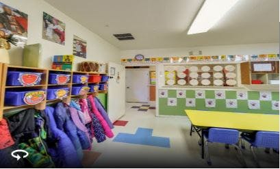 Classroom with cubbies, coats, and a yellow table with blue chairs