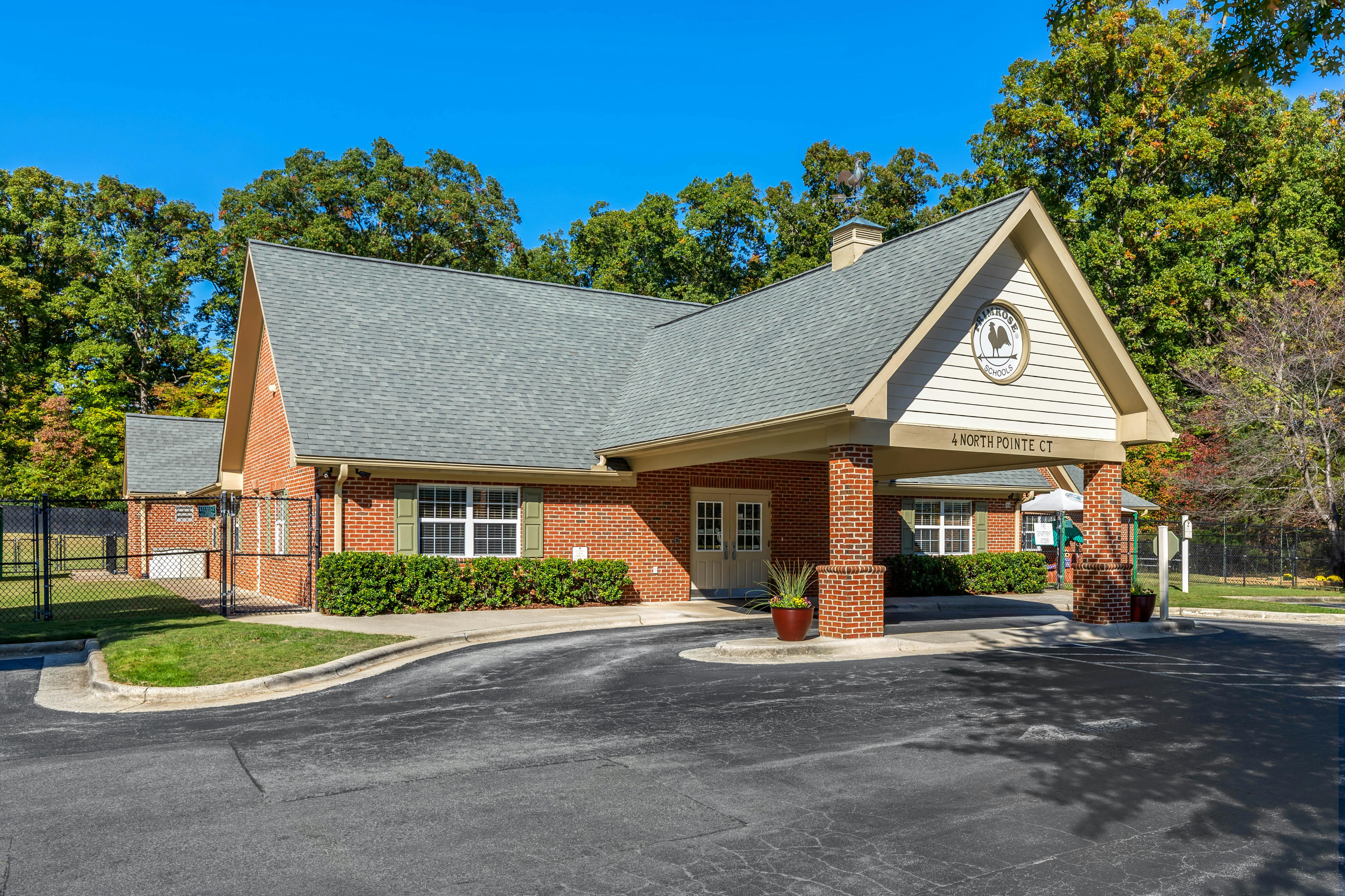 Brick building with a gray roof and covered entrance, surrounded by trees