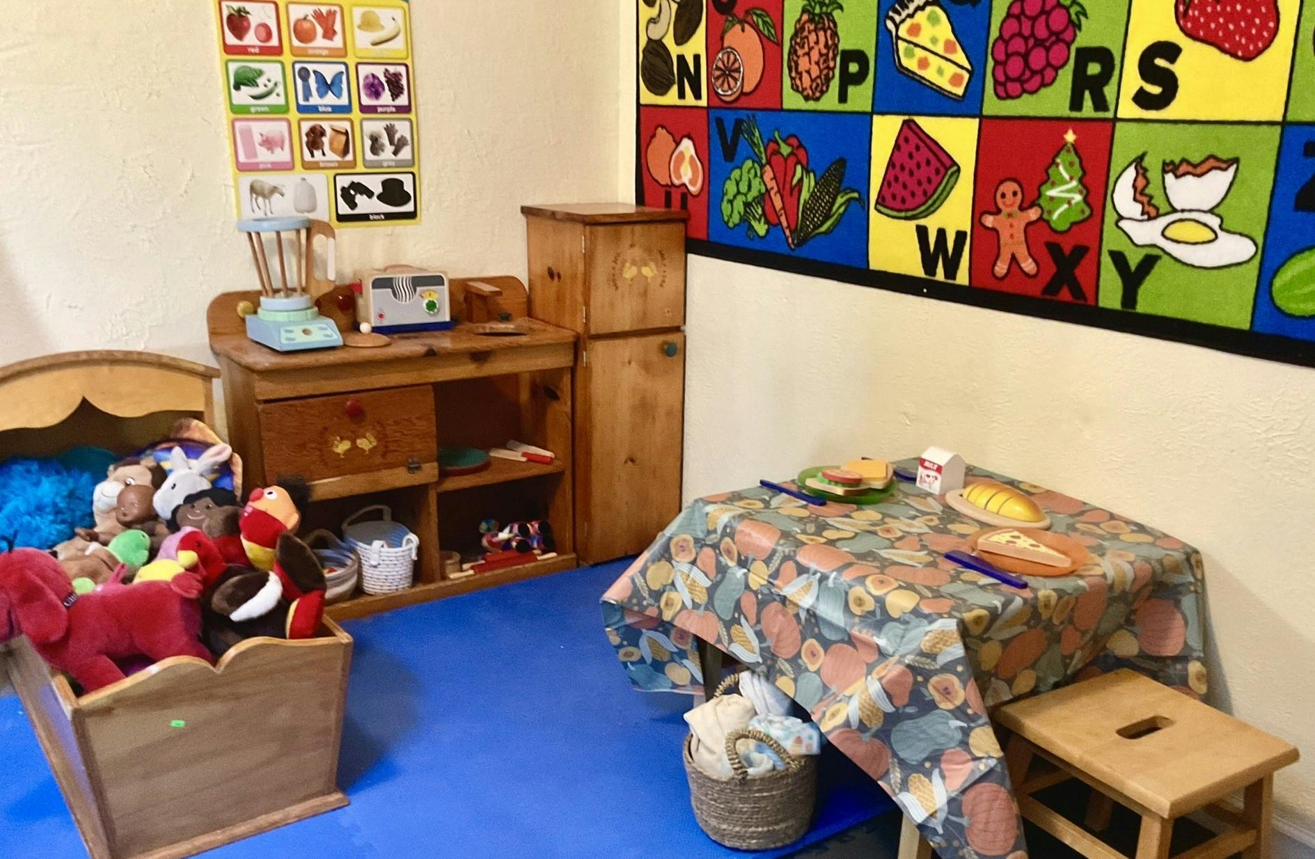 Playroom with toy kitchen, table, and wooden cradle with stuffed animals
