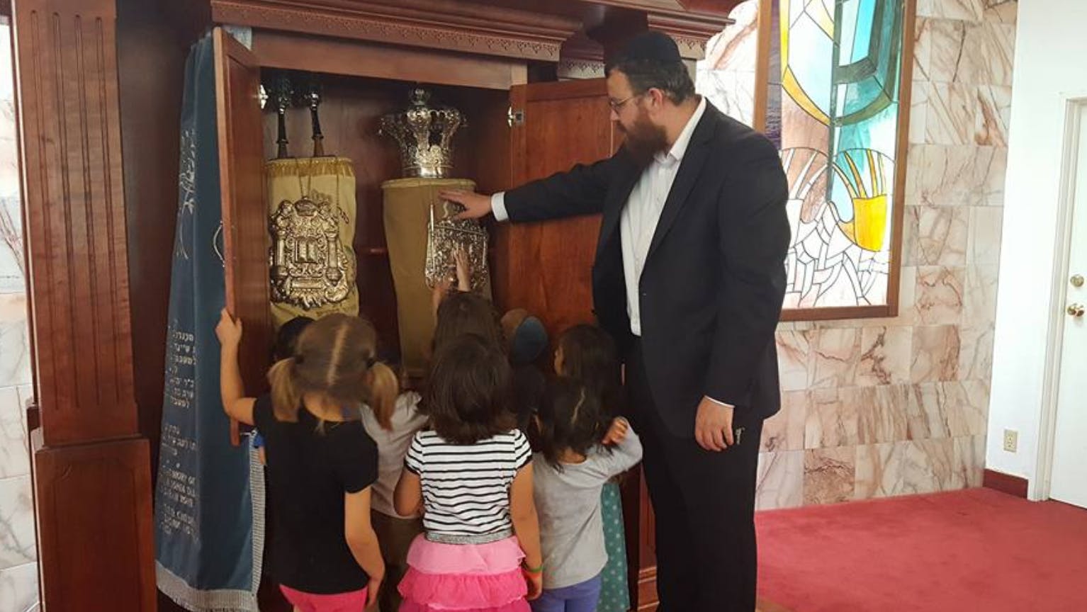 Person and children looking at Torah scrolls in an ark