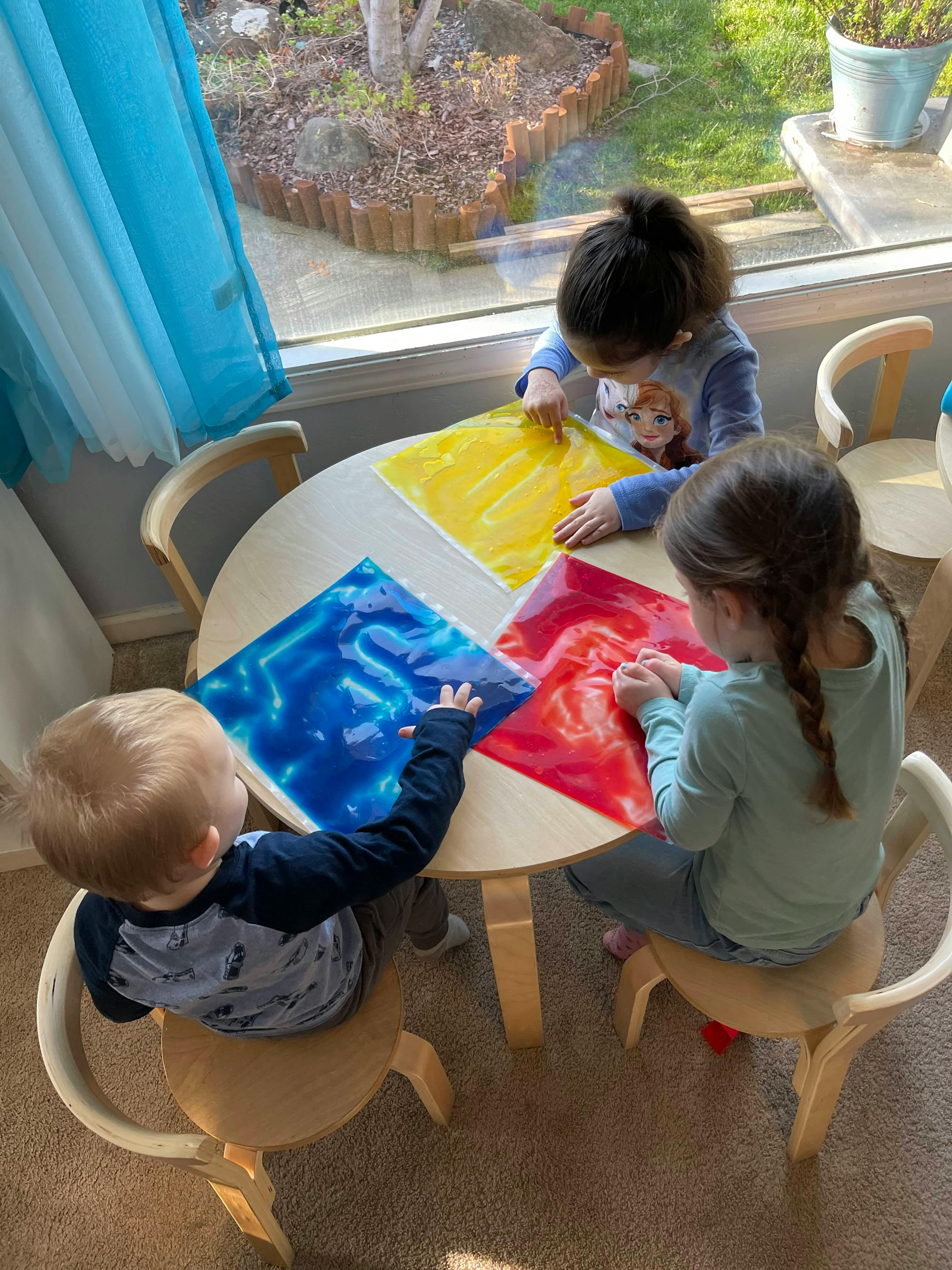 Three children sitting at a round table playing with colorful sensory bags