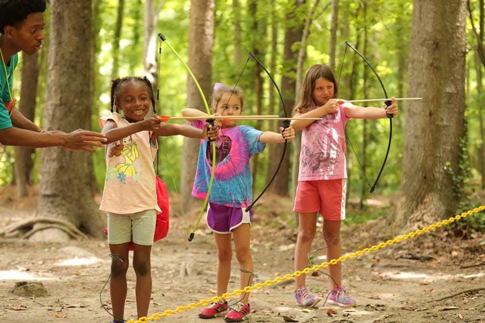 Person teaching three children archery outdoors