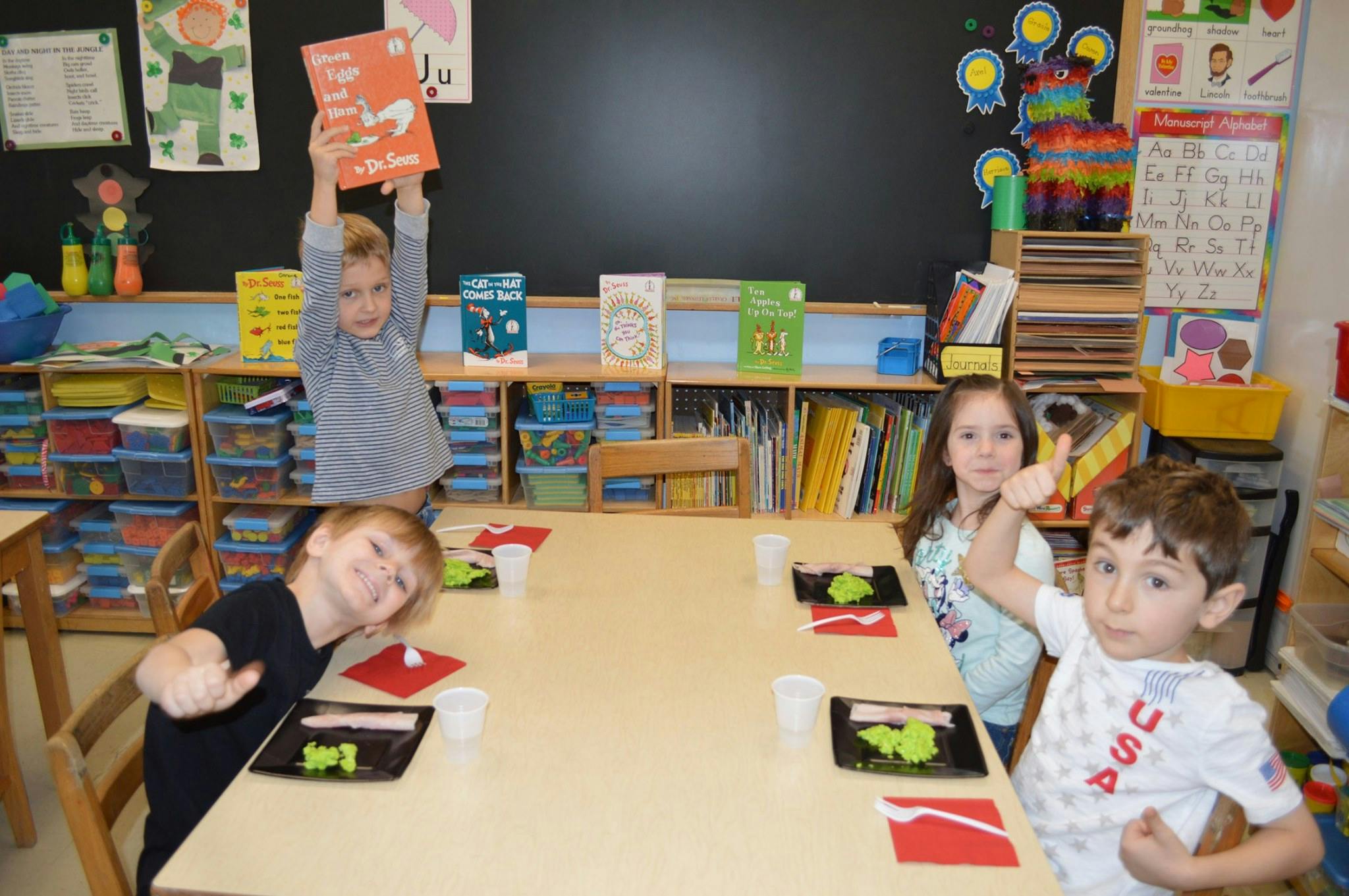 Children in a classroom, one holding a book overhead