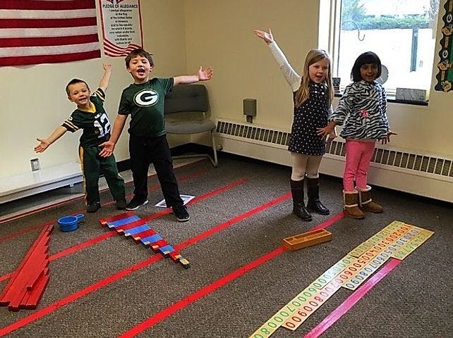Four children standing with arms outstretched in a room with red tape on the floor