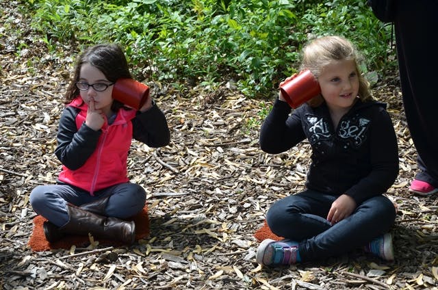 Two children sitting on the ground with red cups to their ears
