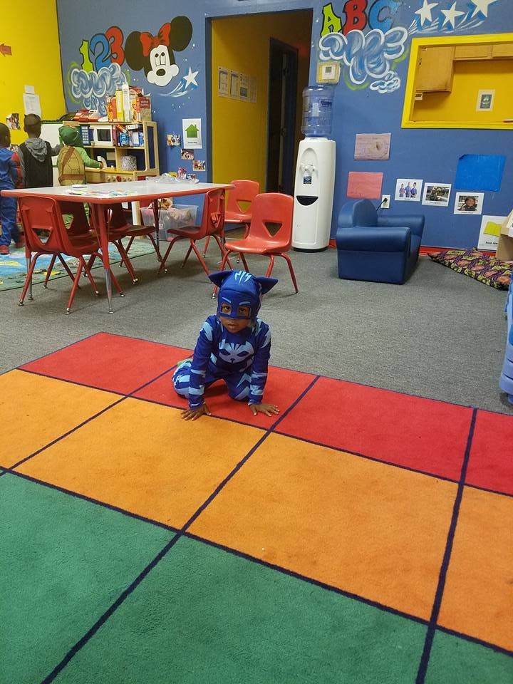 Child in a blue costume kneeling on a colorful rug in a classroom