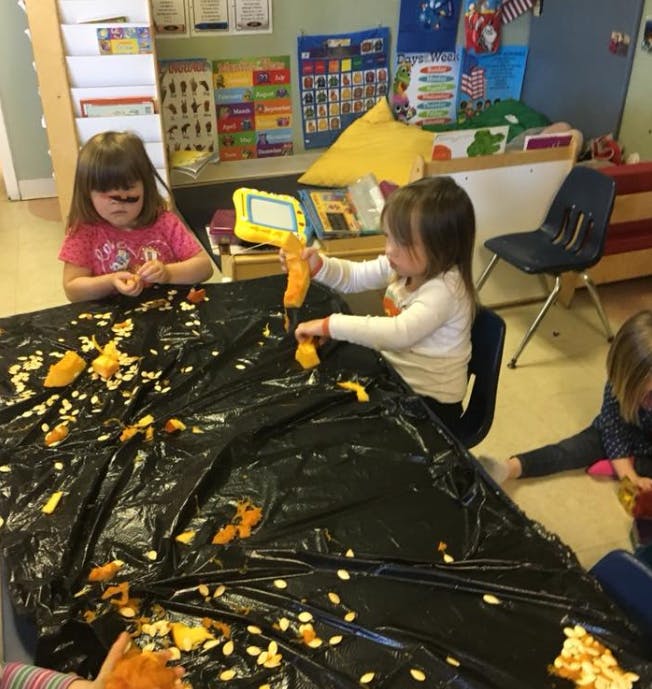 Children playing with pumpkin guts and seeds on a black tarp