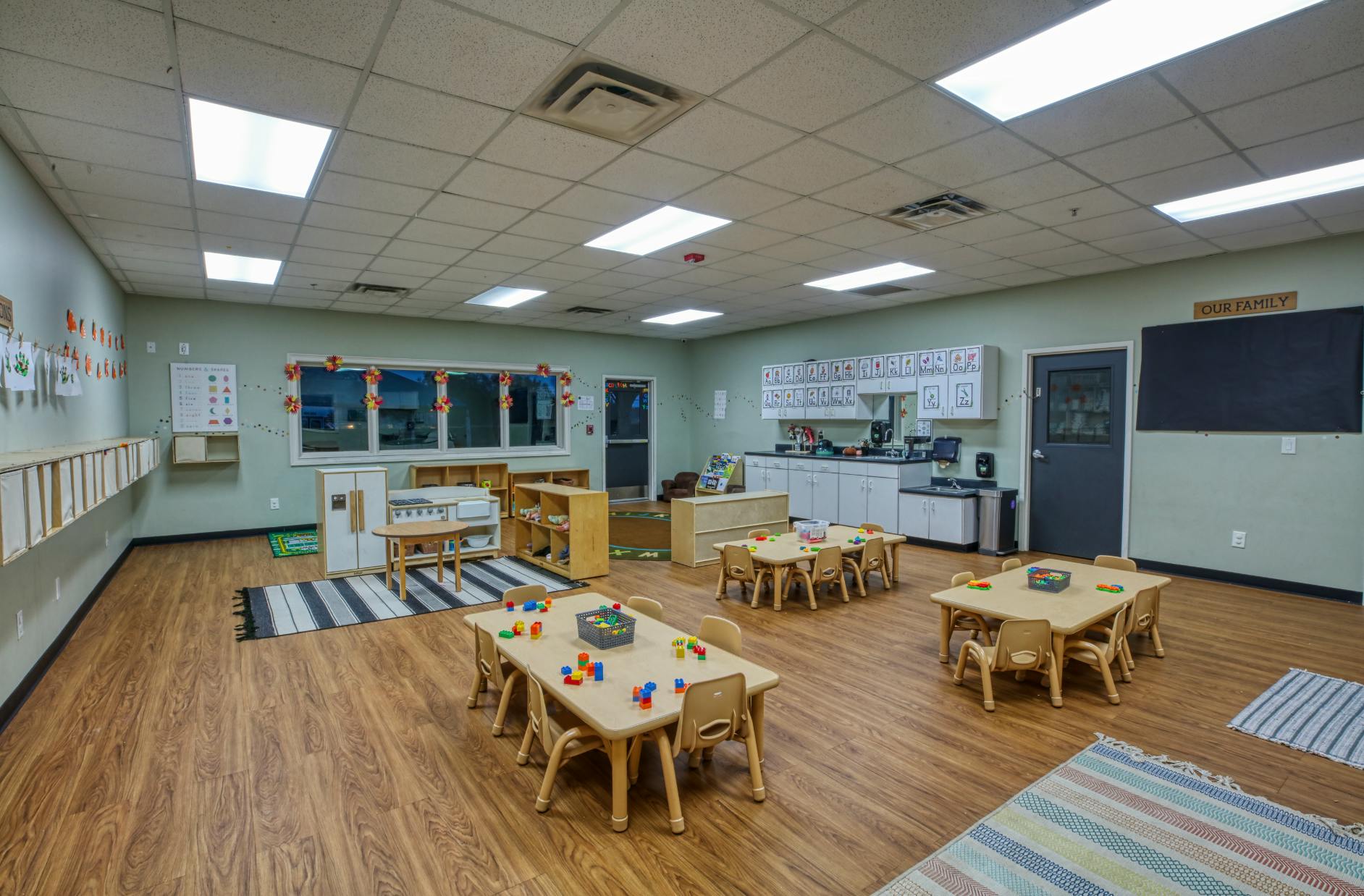 Empty classroom with small tables and chairs, play kitchen, and storage shelves