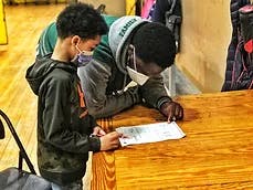 Two teens wearing masks looking at a paper on a table