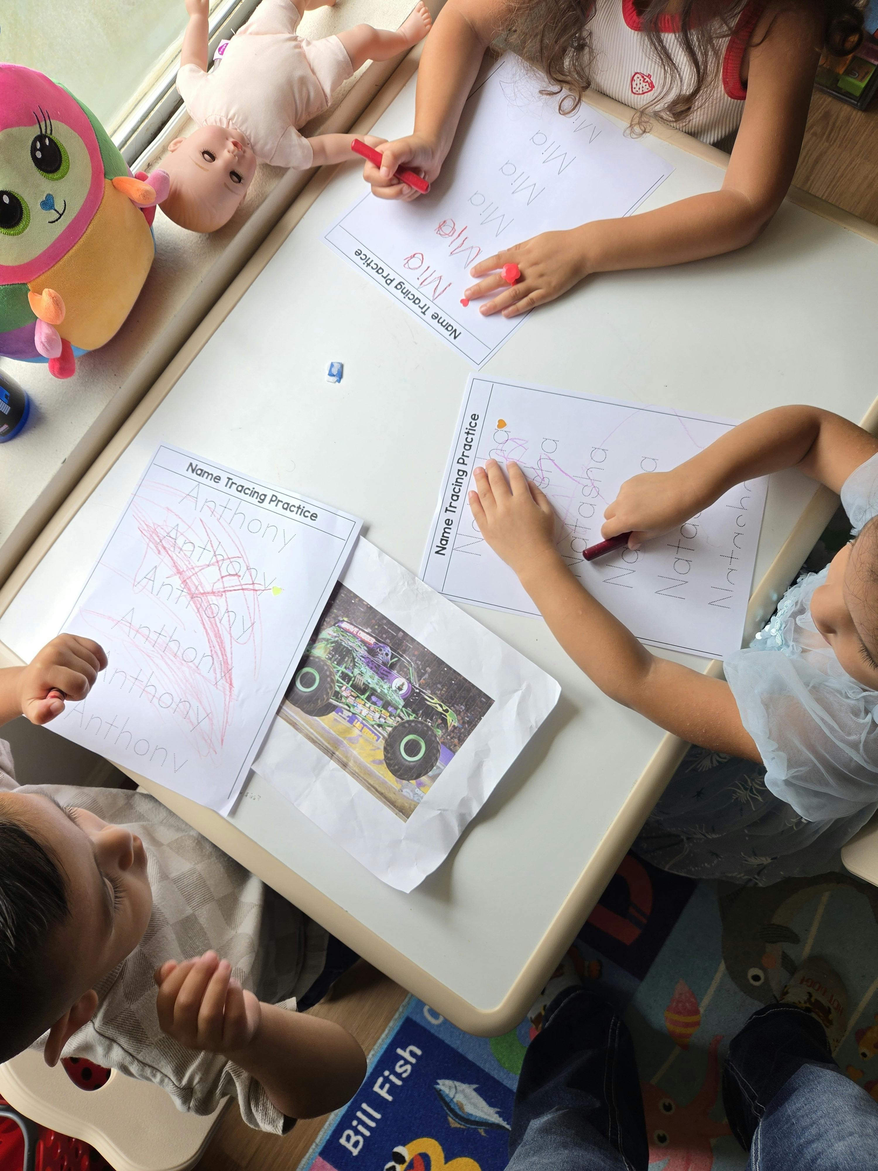 Three children working on name tracing practice worksheets at a table