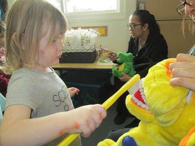 Child brushing teeth of a large stuffed animal with a giant toothbrush