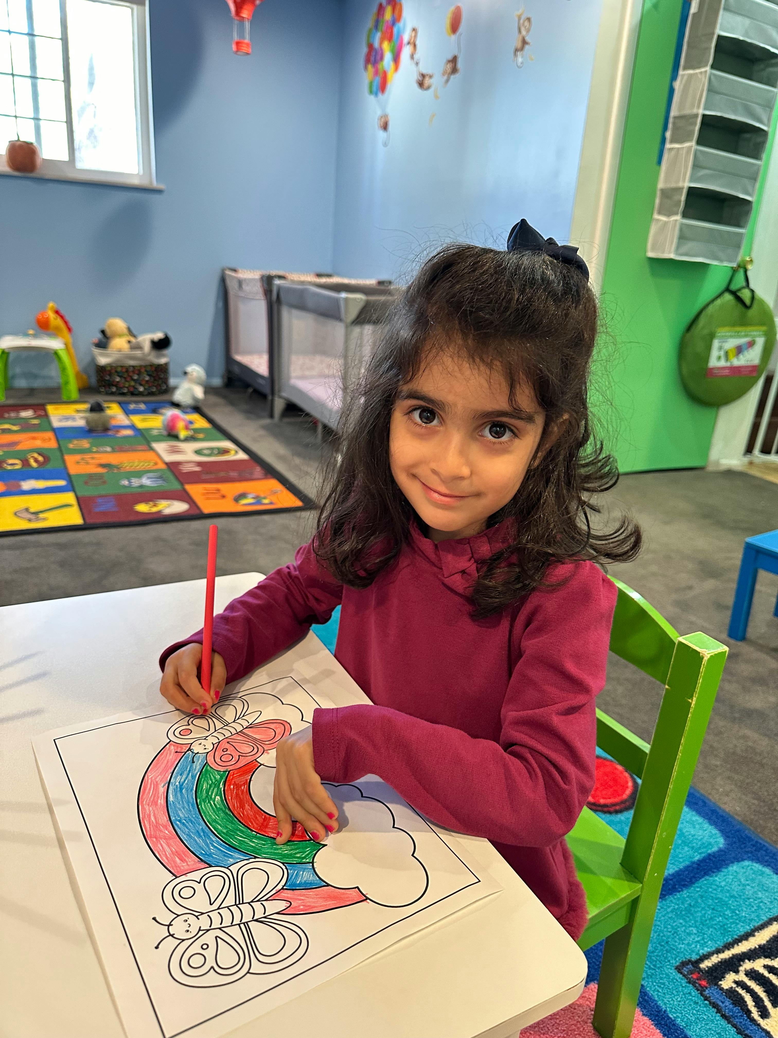 Child coloring a rainbow and butterfly at a table in a classroom