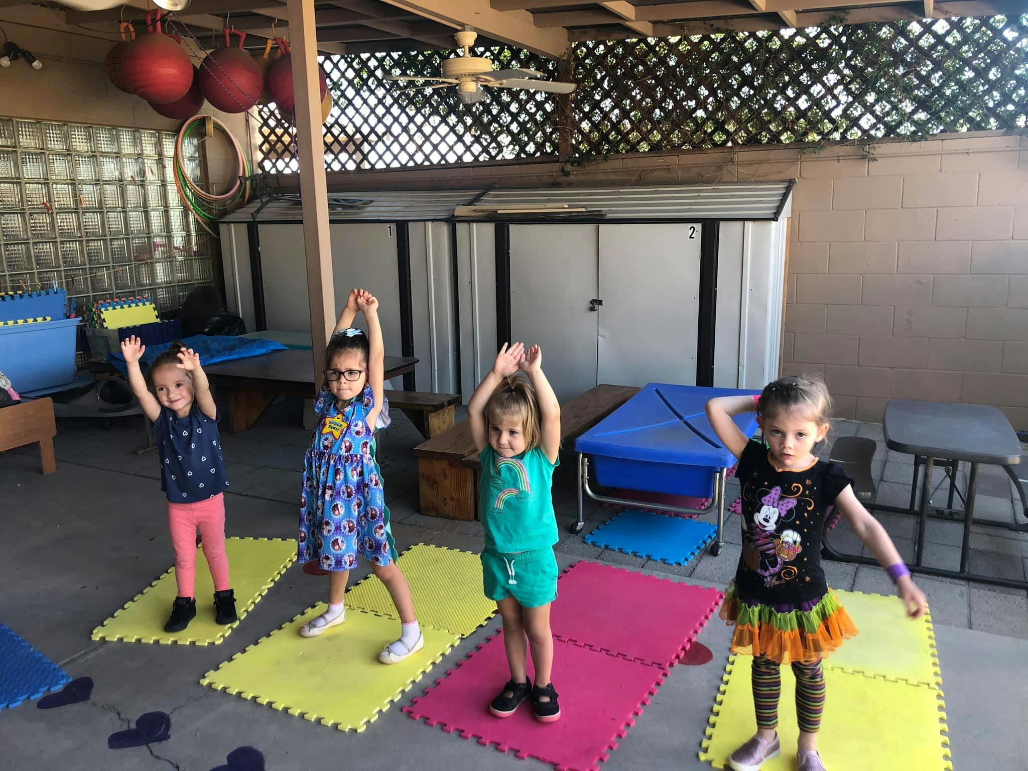 Four children standing on mats with arms raised