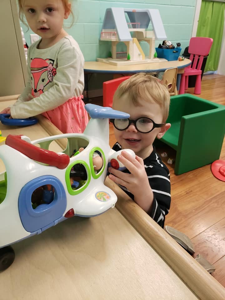 Child in glasses playing with a toy airplane at a table