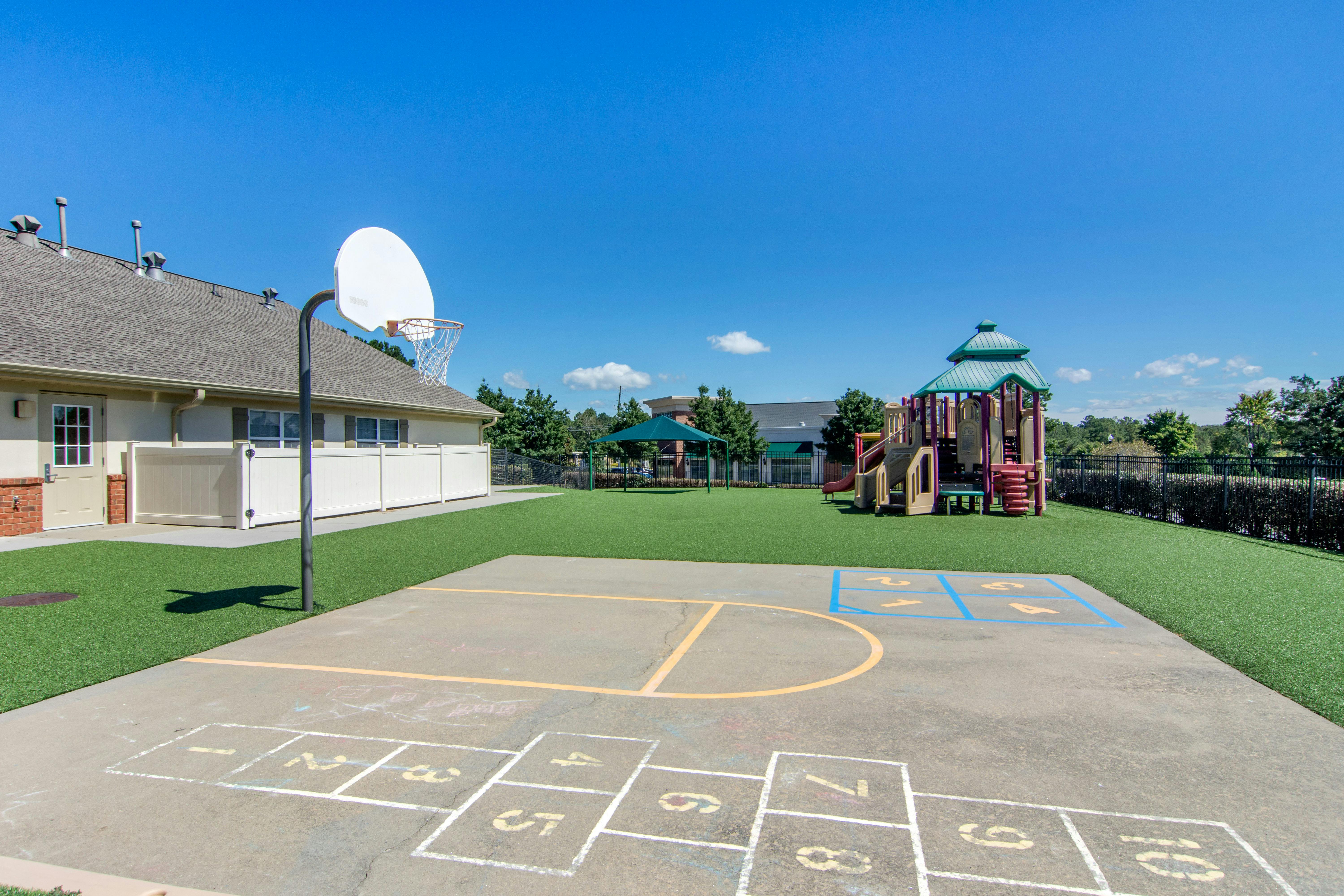 Outdoor play area with hopscotch, basketball hoop, and playground equipment on a sunny day