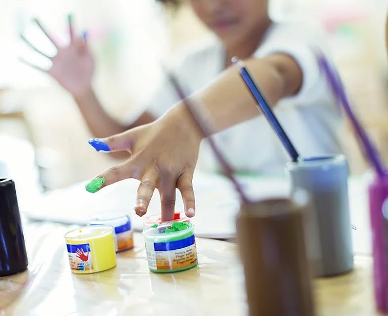 Child with paint on fingers reaching for paint pots