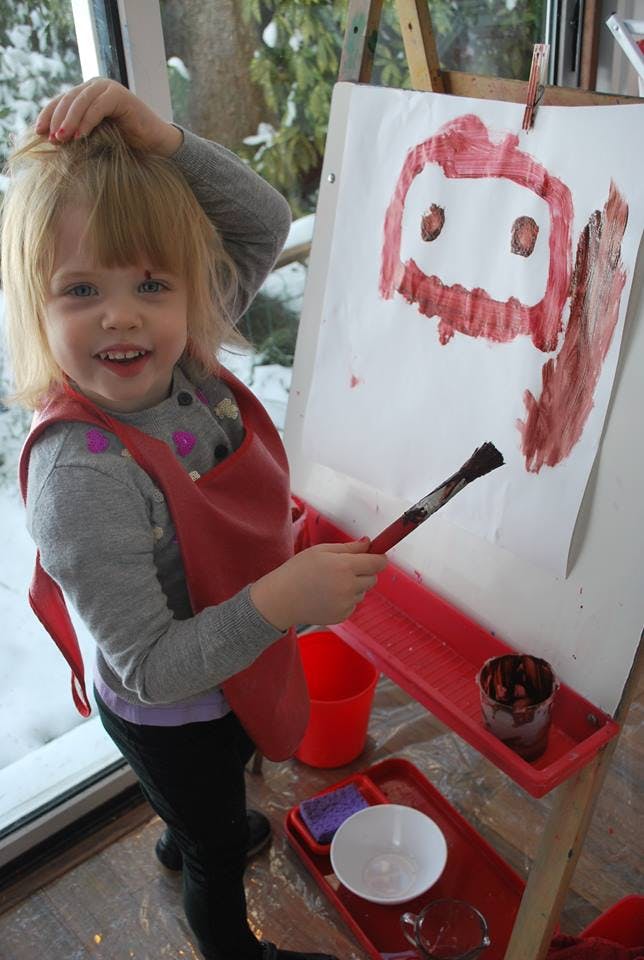 Child in an apron painting on an easel