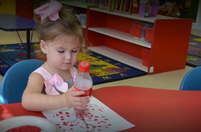 Child holding a bottle over a paper with red dots