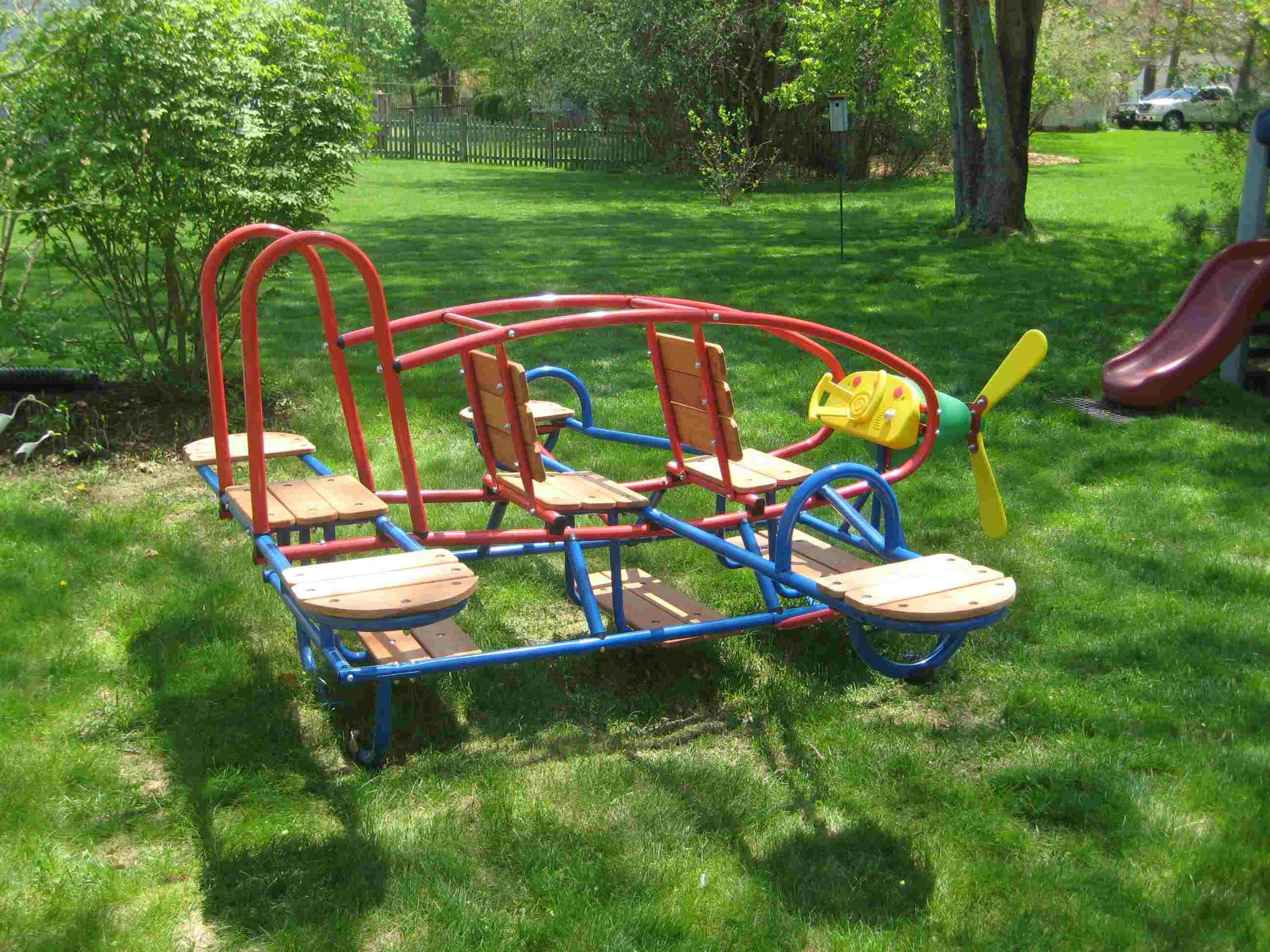 Red and blue metal playground airplane with wooden seats on grass
