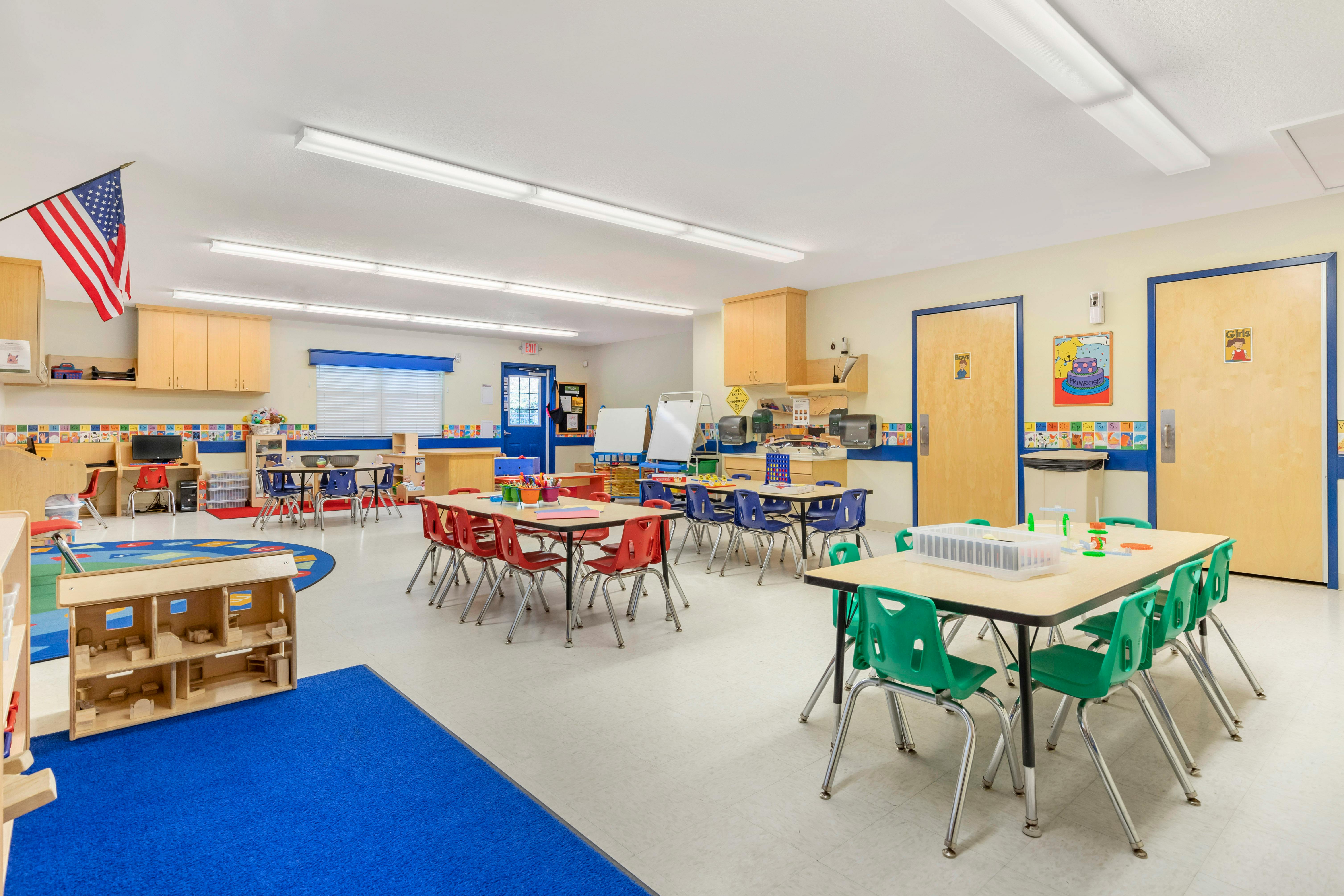 Classroom with multiple tables and chairs, a play area, and an American flag