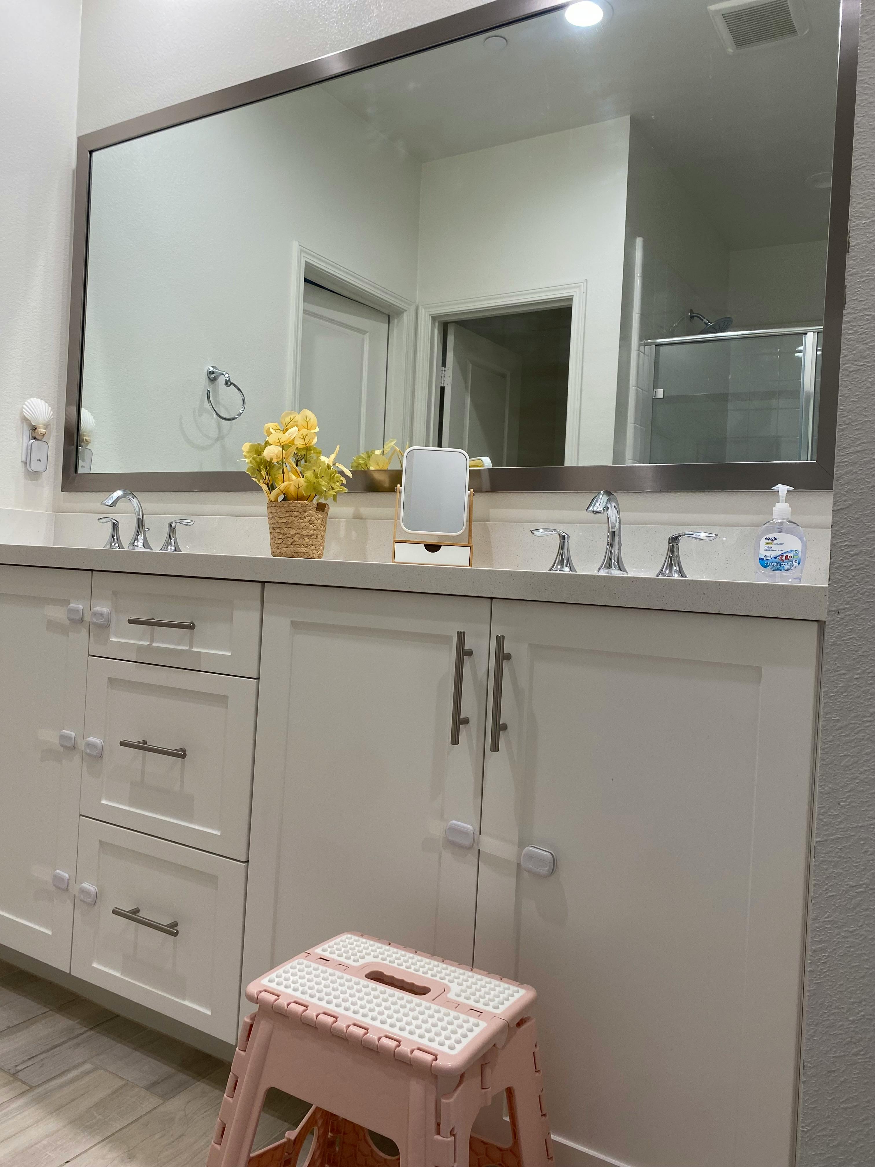 Bathroom vanity with two sinks, a large mirror, and a step stool