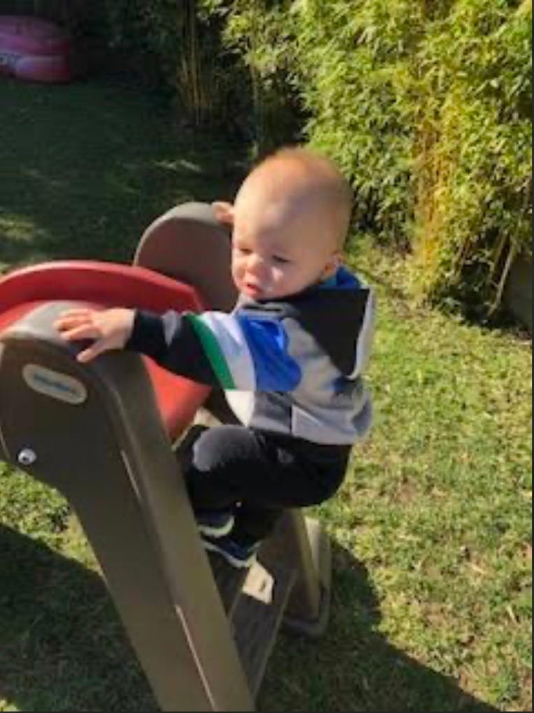 Child climbing a small plastic slide in a yard