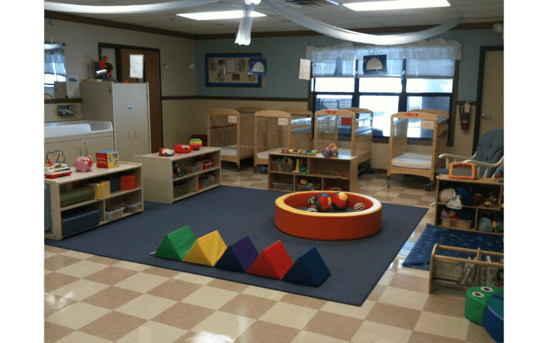 A colorful room in a daycare center with several cribs, play mats, and toys