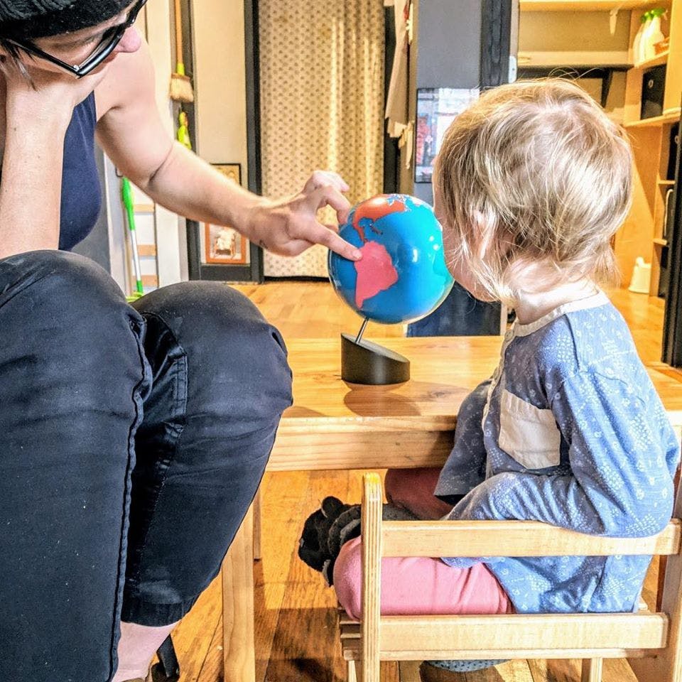 Person pointing at a globe while a child watches