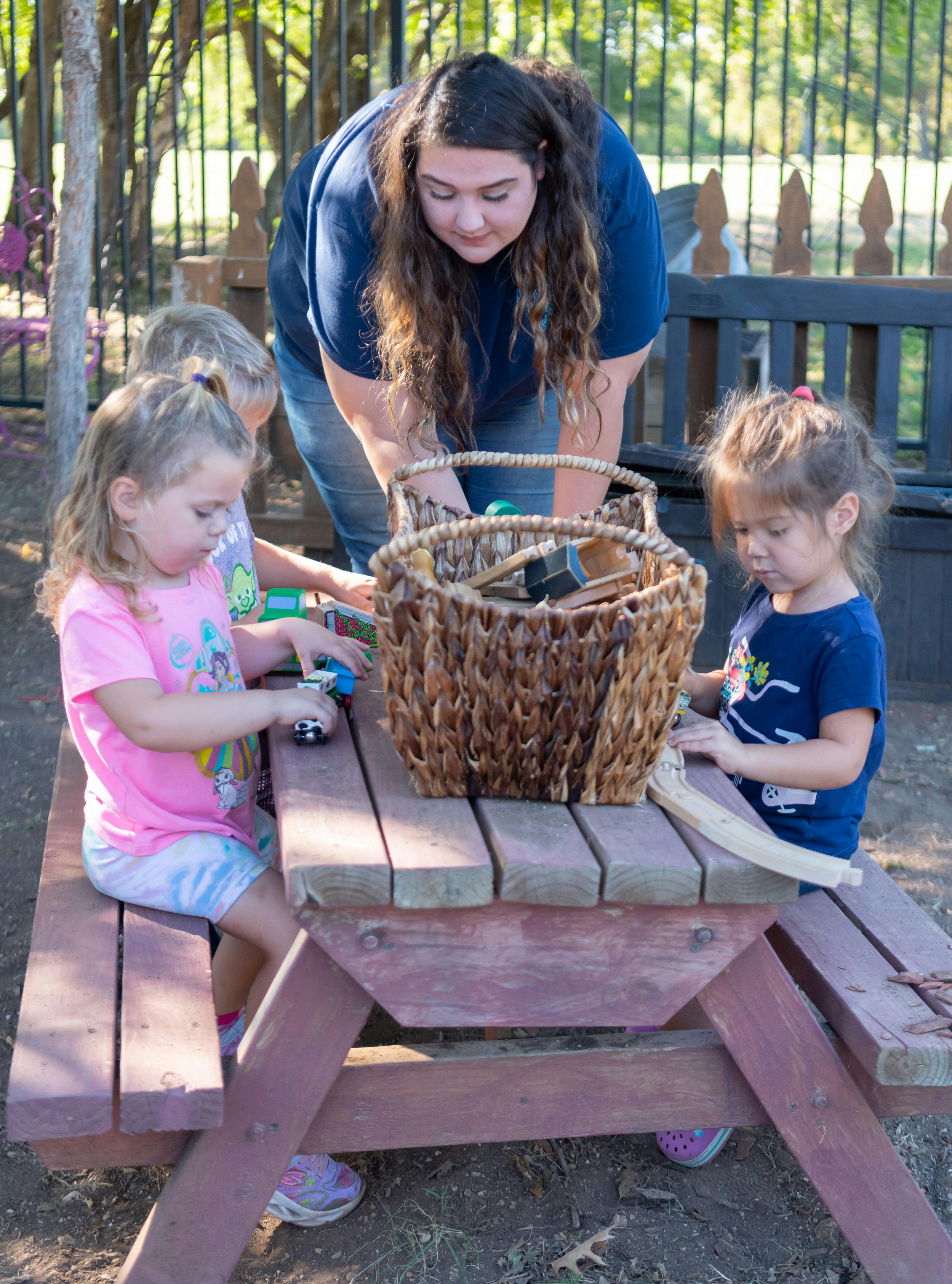 Adult and two children playing with items on a picnic table