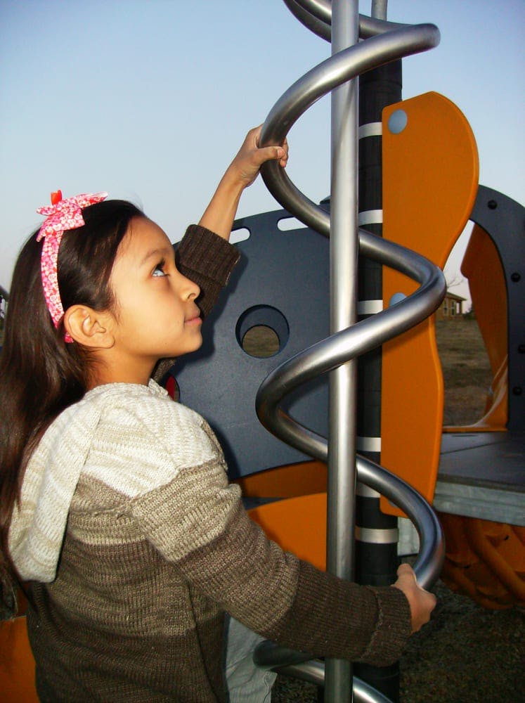 Child on a playground holding onto a spiral pole