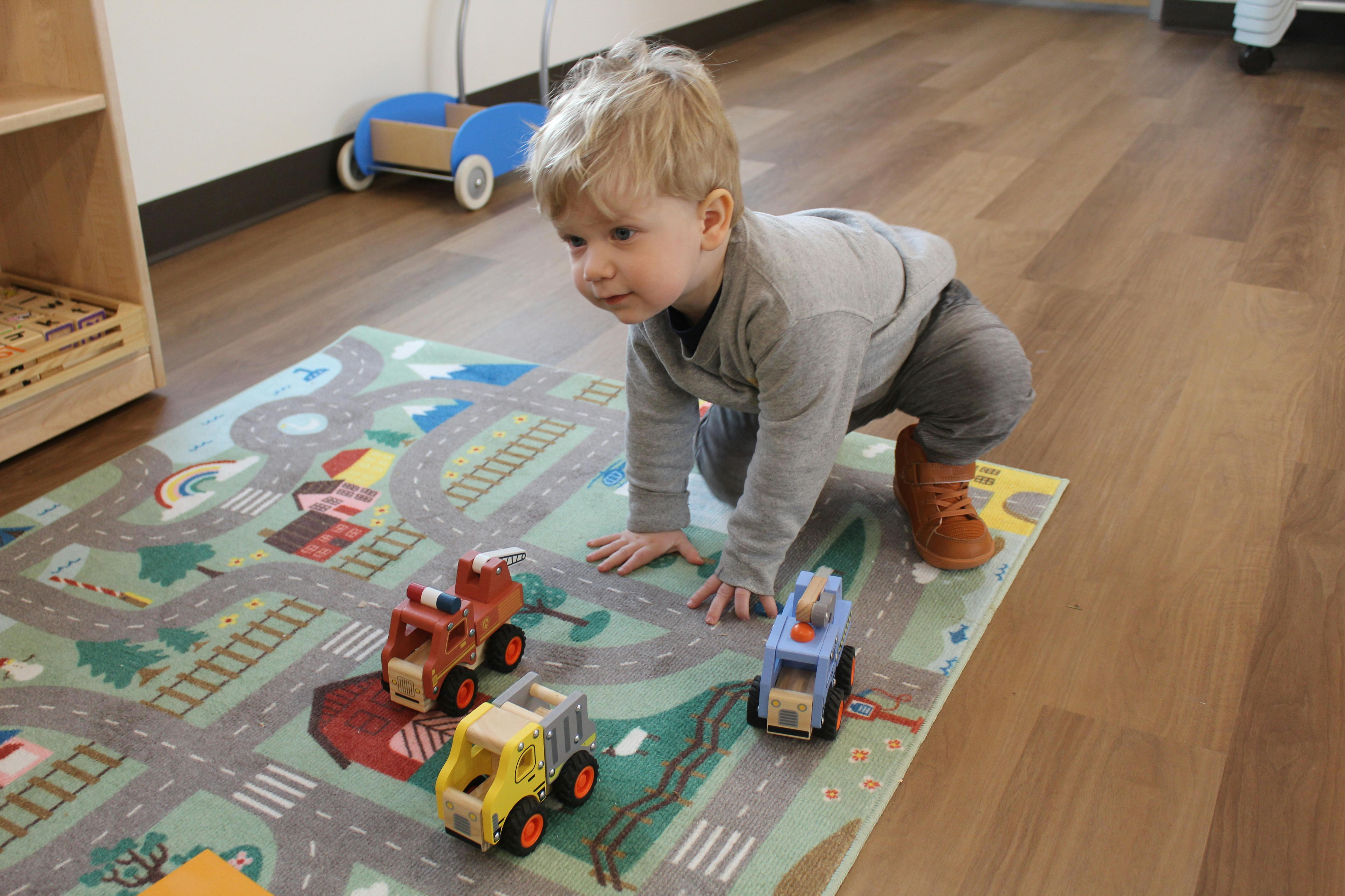 Child on hands and knees on a playmat with toy trucks
