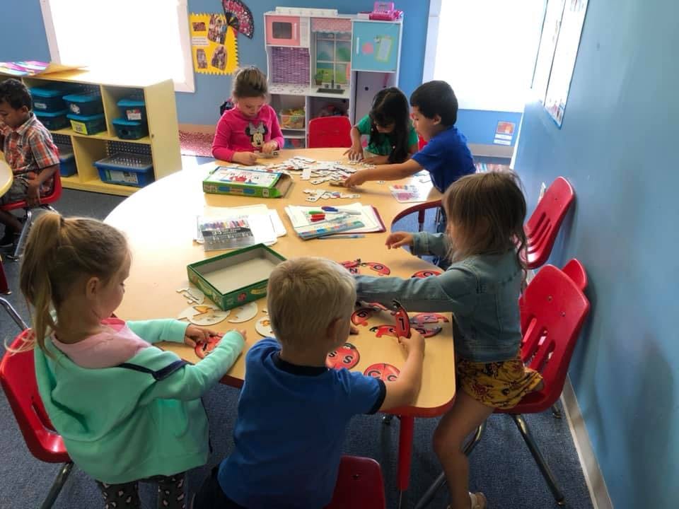 Children sitting at a table playing with puzzles in a classroom