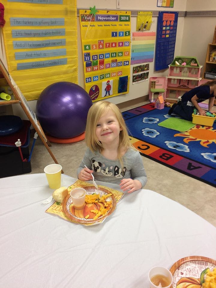 Child sitting at a table with a plate of food in a classroom