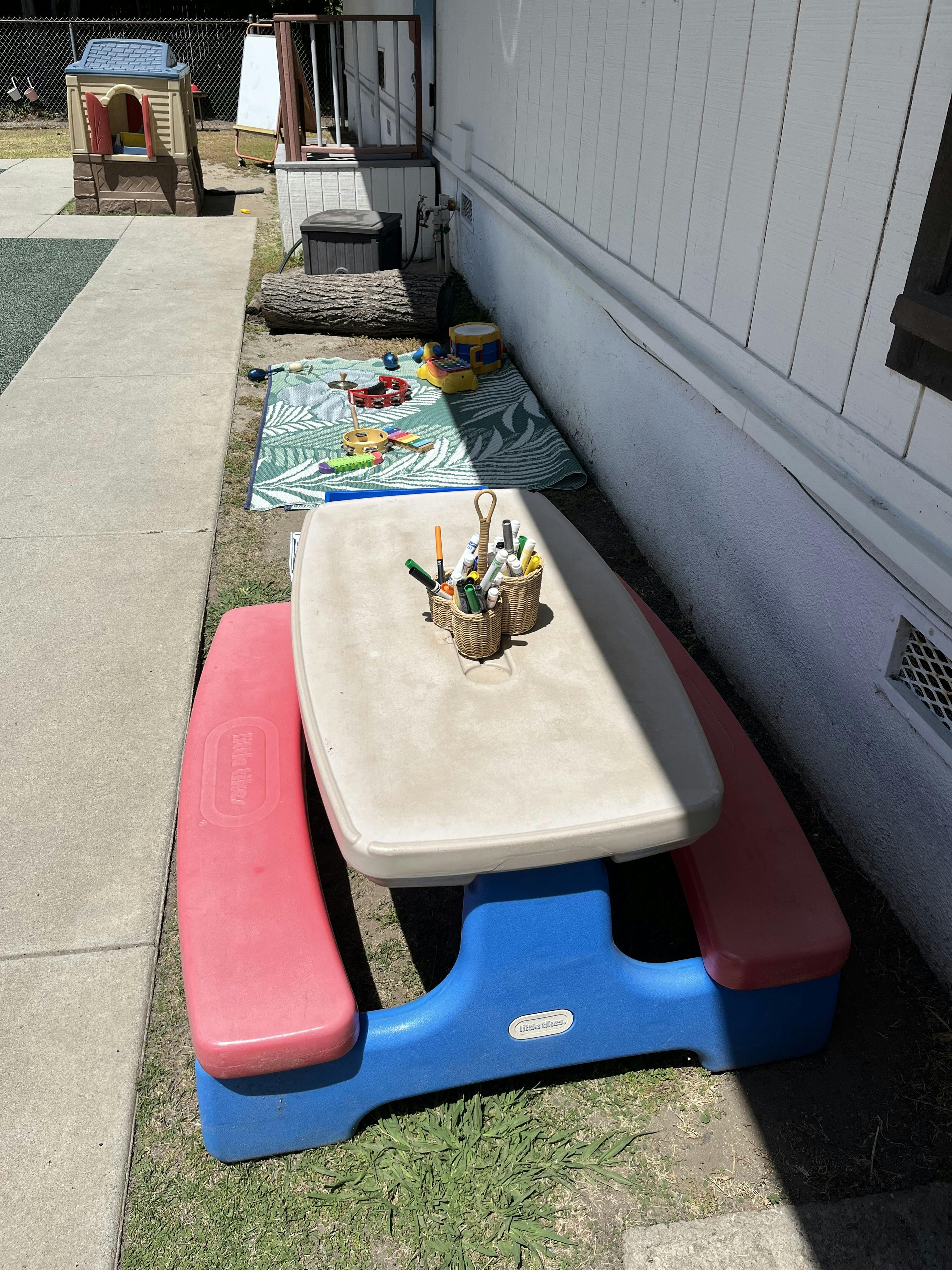 Child-sized picnic table with craft supplies and toys on a mat in a play area