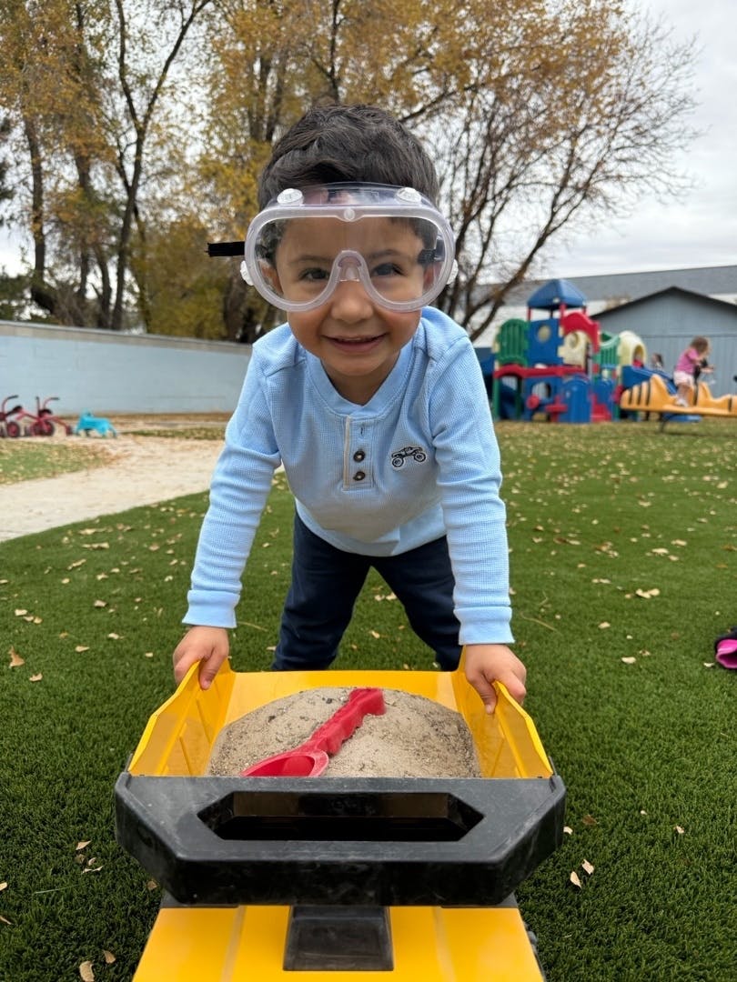 Child wearing goggles and pushing a toy truck full of sand