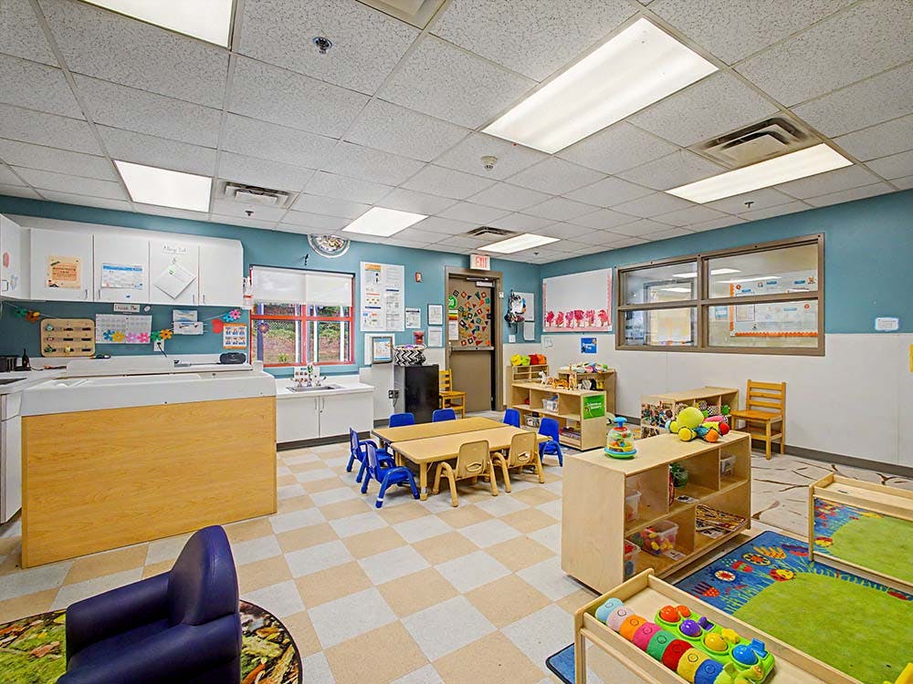 Empty children's classroom with small tables, chairs, and play equipment