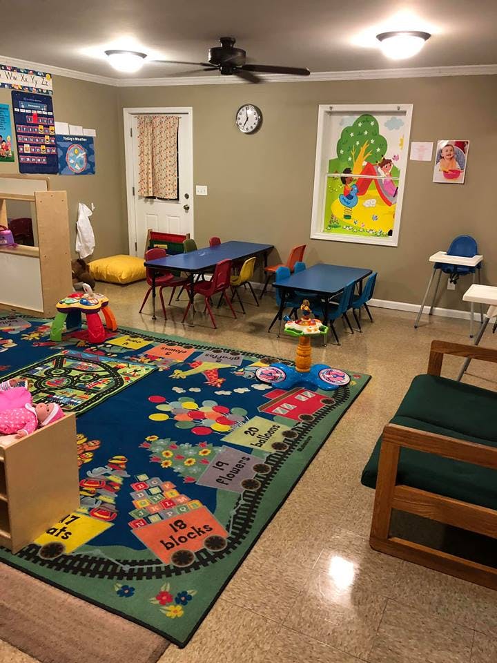 A classroom with small tables and chairs, a colorful rug, and a crib