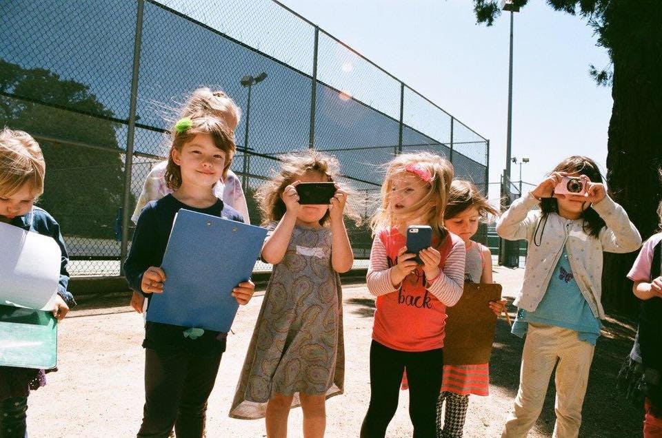 Children holding cameras and a folder outdoors
