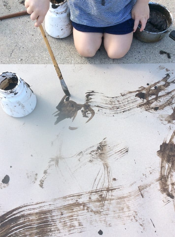 Child kneeling and painting with mud on a large white surface