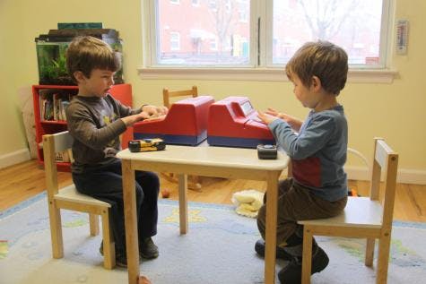 Two children playing with toy cash registers at a small table