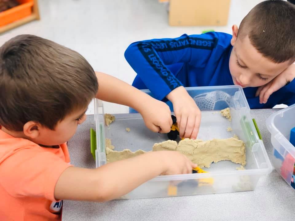 Two children playing with kinetic sand in a classroom