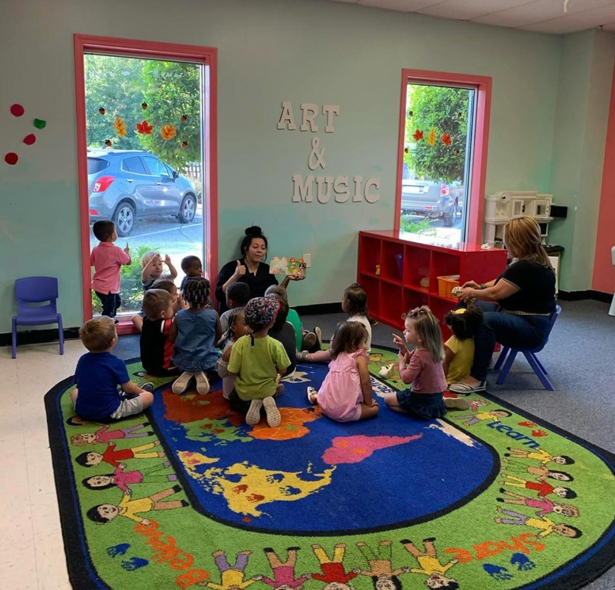 People reading a book to children in a classroom with a map rug
