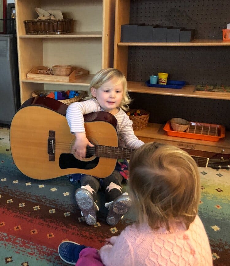 Child playing a guitar for another child