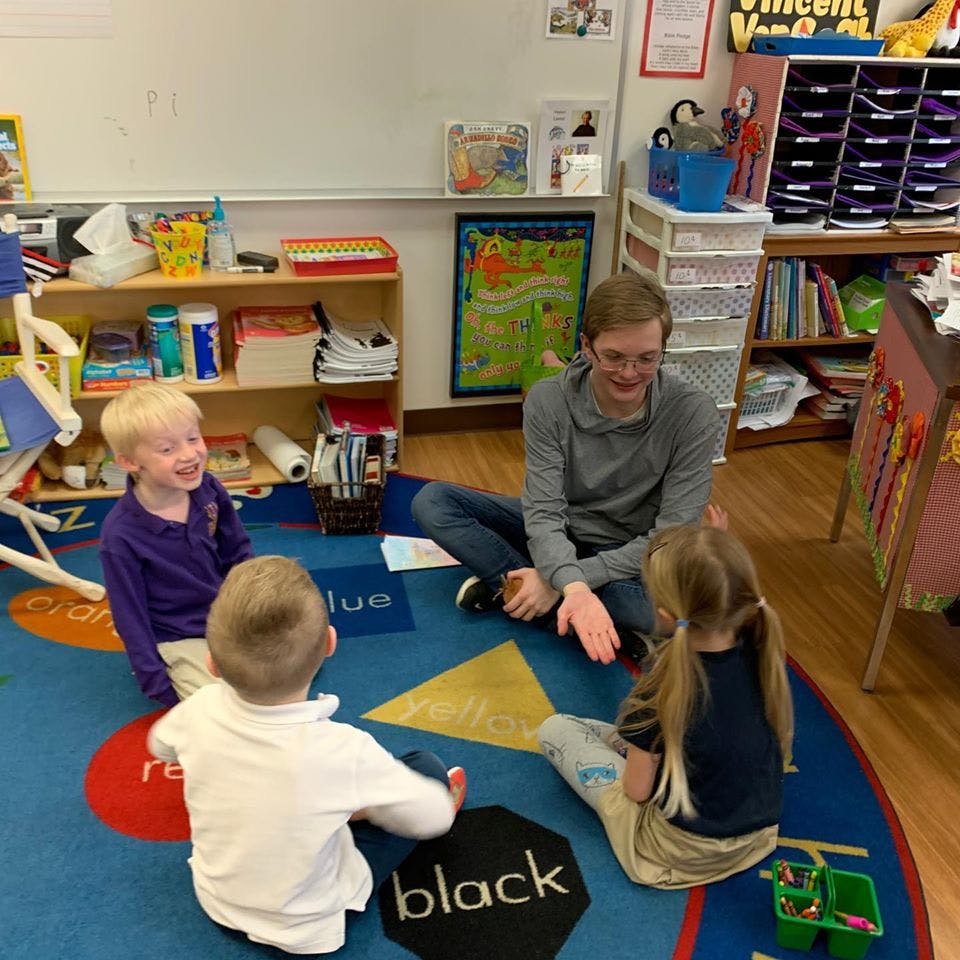 Adult and three children sitting on a rug in a classroom