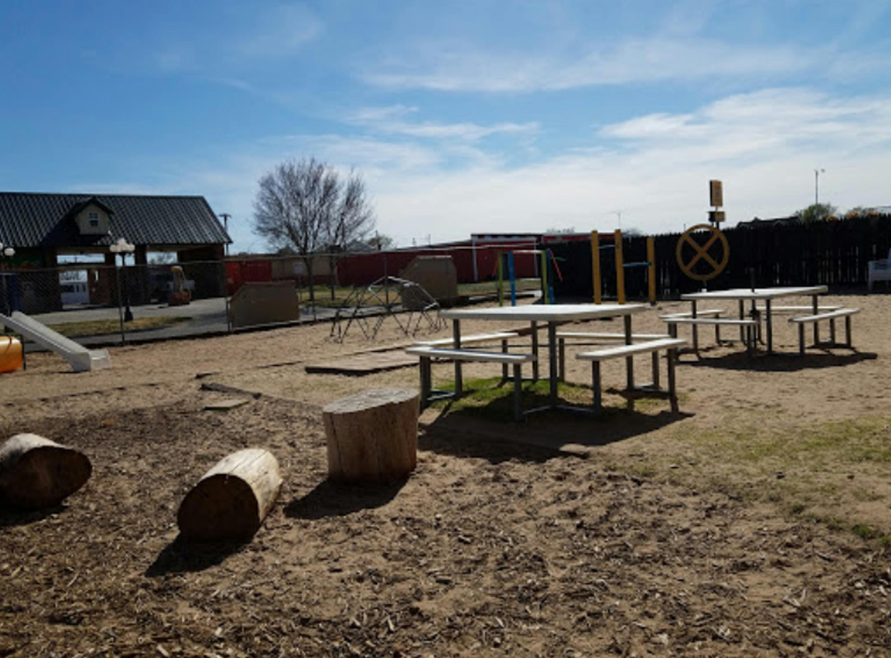 Picnic tables and playground equipment on a dirt and grass area