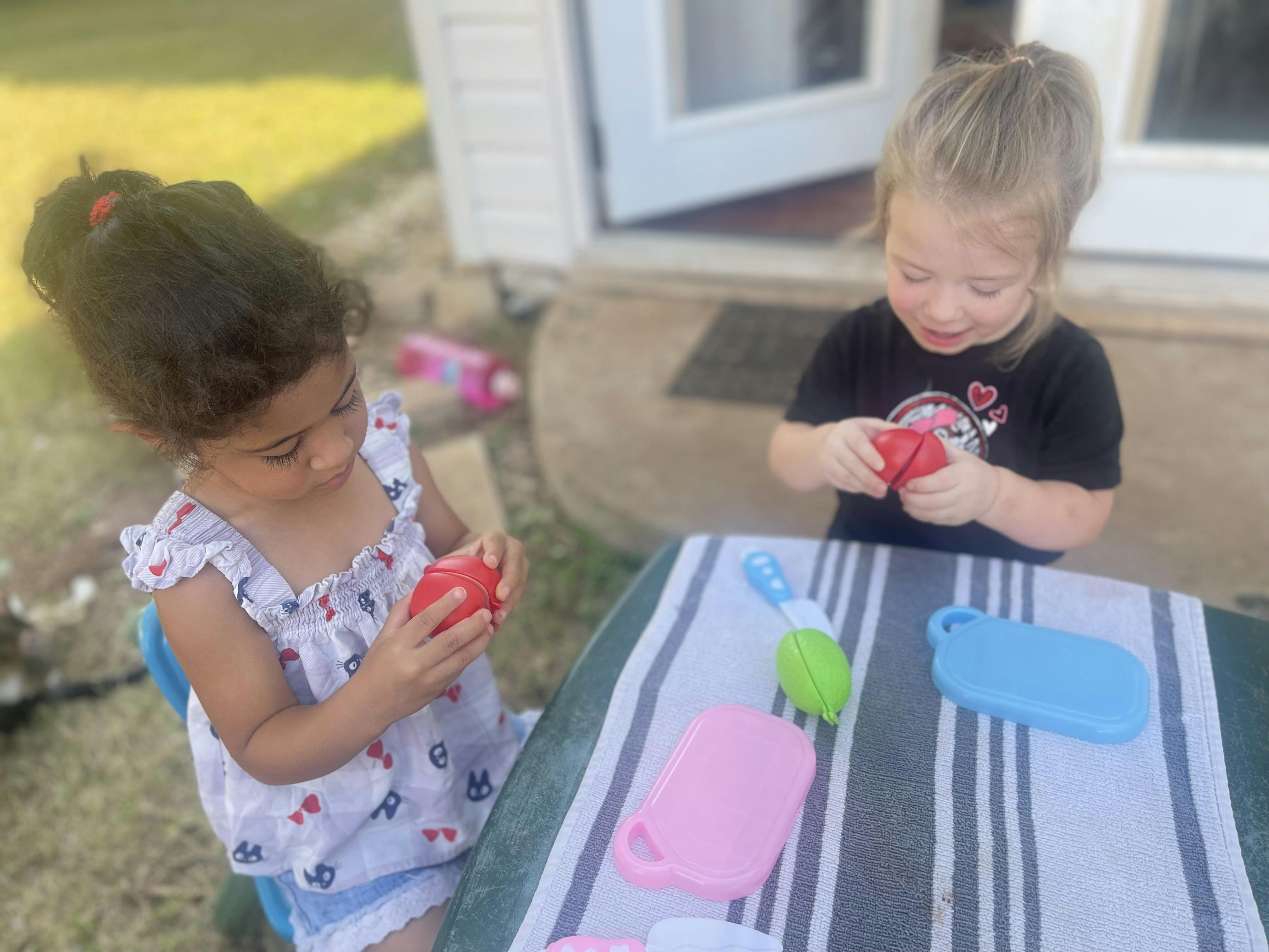 Two children playing with toys at a table outdoors