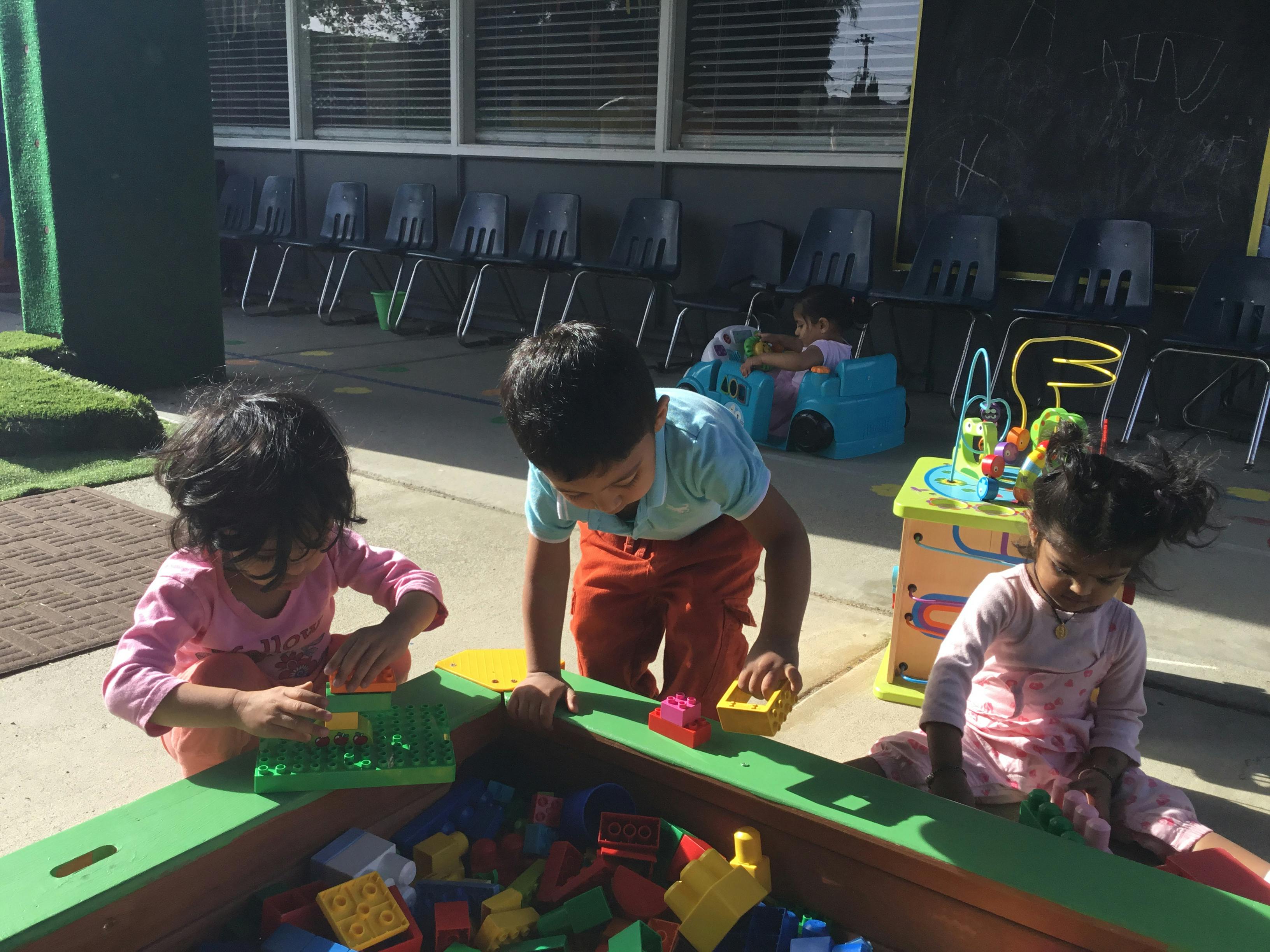Three children playing with blocks and toys outdoors