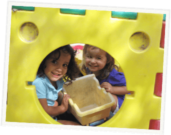 Two children looking through an opening in a yellow play structure