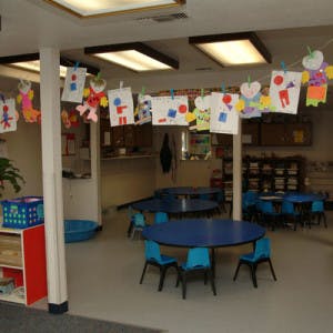 Children's artwork hanging in a classroom with small tables and chairs